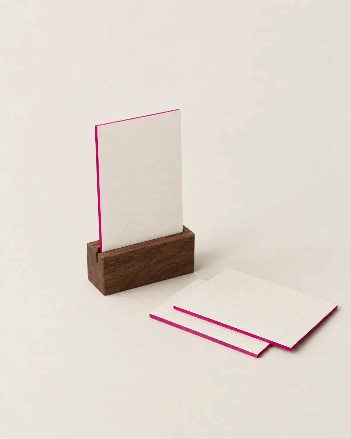 A blank cream card with magenta edges standing in a walnut holder.